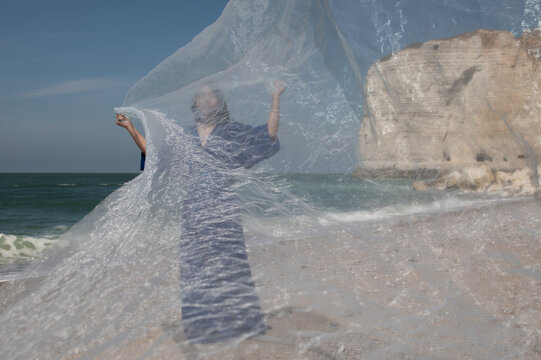 woman in blue dress holding thin fabric near on the beach of Etretat, Normandy, France