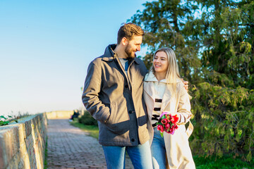 A young couple in love is walking, she is carrying a bouquet of flowers.