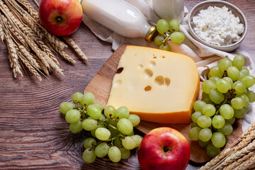 Shavuot flat lay with dairy products, first fruits and wheat on brown wooden background