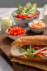 Banh Mi - Vietnamese sandwich with sausage, pork, lettuce, tomato and arugula on the light grey texture background. One of the most famous street food in the world