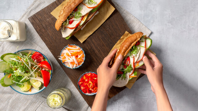 Banh Mi - Vietnamese sandwich with sausage, pork, lettuce, tomato and arugula on the light grey texture background. One of the most famous street food in the world