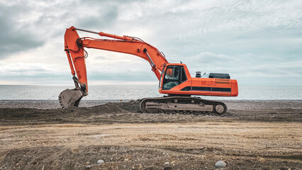 orange excavator by the sea