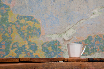White mug standing on top of old wooden table. In the background a colorful, cracked wall. Rustic interior.