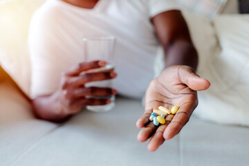 Unrecognizable African American man ready to take a pill while lying in bed. Shot of an young man...