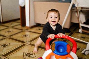 Cute baby boy with toy walker at home interior