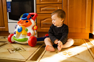 Cute baby boy with toy walker at home interior