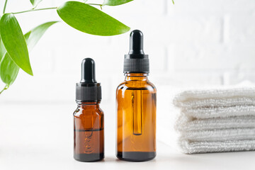Natural organic cosmetic concept. Two dark glass bottles of cosmetic product on whine background with green leaves and stack of white spa towels. Mock up of product.close up.