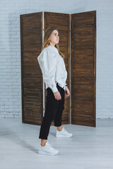 A beautiful stylish woman is wearing a white cotton shirt and black pants. Cheerful emotional girl in white sneakers