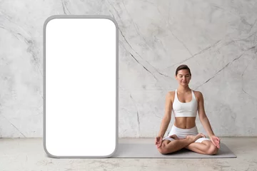 Fotobehang Young woman practicing yoga in lotus pose over textured wall with giant phone screen © Damir Khabirov