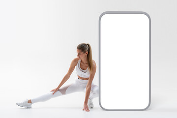 Healthy woman warming up, squatting and stretching leg with big phone banner with copy space