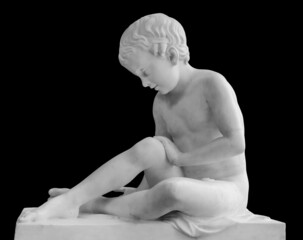 Ancient marble statue of a sitting boy. Young man sculpture isolated on black background. Antique...