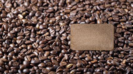 Blank vintage cardboard tag on dark brown background of coffee beans.