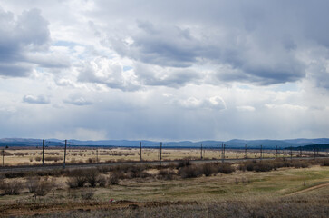 The railroad passes through the field. In the background are mountains and a forest in the distance.