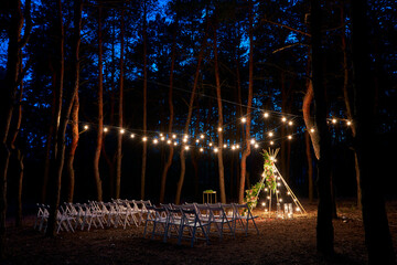 Festive string lights illumination on boho tipi arch decor on outdoor wedding ceremony venue in...