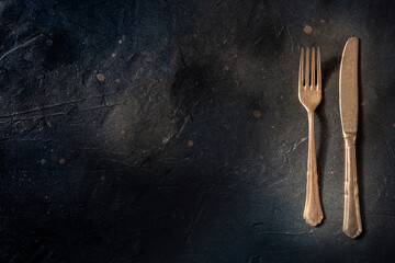 Cutlery. A fork and a knife on a black slate background. Modern tableware on a dark table with a...