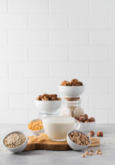 Vegetable milk in a mug on the background of bowls with nuts, oatmeal and legumes. An alternative to dairy products.