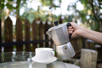 Lady hand pouring freshly brew coffee with Moka Pot with blur country side forest background....