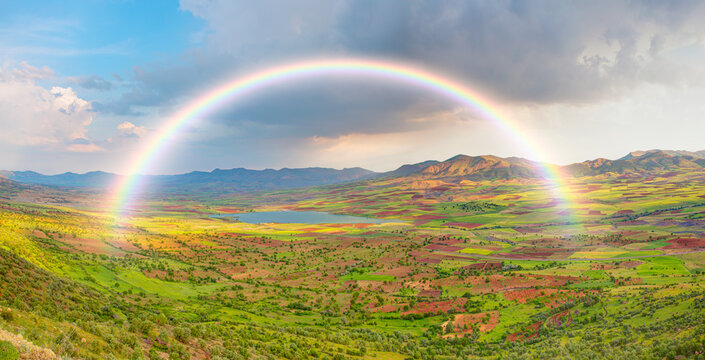 Beautiful blue lake landscape with a view of the mountains and a green valley and a rainbow in the clouds