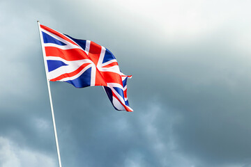 Great Britain England flag waving in the wind over cloudy grey sky low angle view close up.