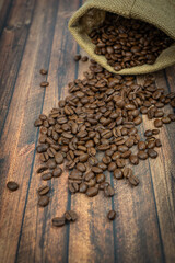 Roasted coffee beans falling from a sack onto a wooden table