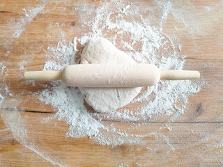 Wooden rolling pin and dough stretched on wooden table. Top view.