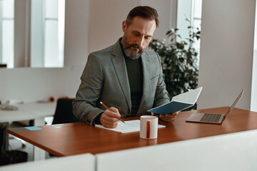 Focused man in casual clothes making notes in notepad while sitting in his office