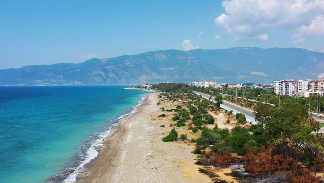 aerial drone panning low across a highway towards a white sandy tropical beach with the Mediterranean Sea and a coastal beach town in Finike Turkey on a sunny summer day