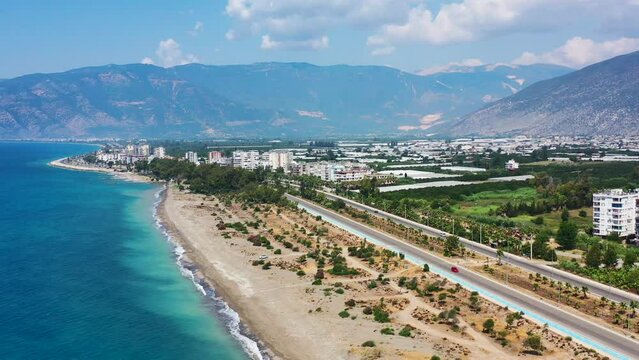Aerial view of a white sandy tropical beach in Finike Turkey on a sunny summer day with an empty highway road leading to a beach town with mountains in the distance