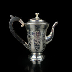antique metal teapot. silver tea service. metal jug with engraving on a black isolated background