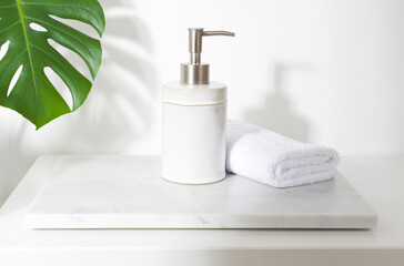 Fototapeta na wymiar Ceramic soap dispenser and folded towel on white marble stand