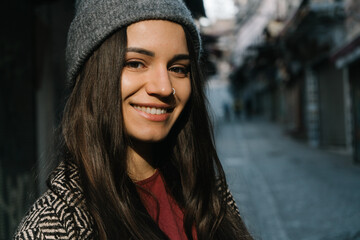 A girl with dark straight long hair in a gray coat, hat and burgundy T-shirt. Portrait of a happy...