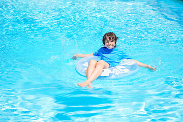 Fototapeta na wymiar Boy relaxing on an inflatable swim ring in a sunny day, spending time in a swimming pool, aquapark resort hotel. Summer holidays concept.