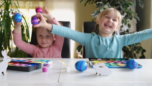Happy preschool cute kids having fun looking into the camera making crazy funny face with colored Easter eggs at home.