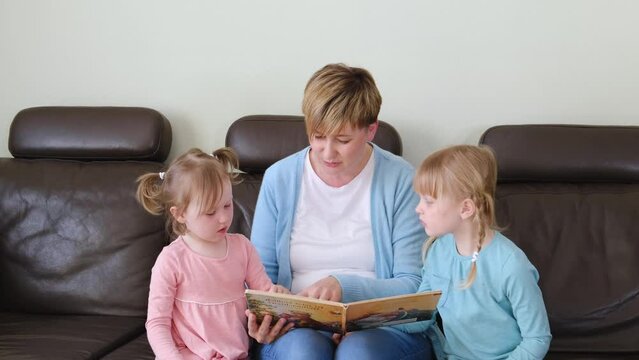 Mother and preschool cute daughters having fun at home, eading fascinating fairy tale book.