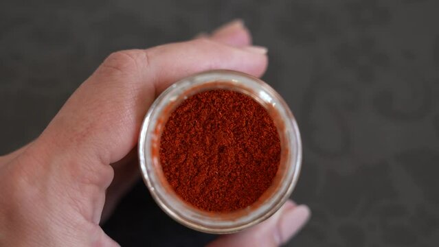 Close-up view 4k stock video footage of grounded into powder red smoked paprika pepper isolated in glass container. Woman holding glass bottle full of fry grounded powder red pepper spices