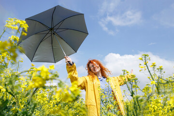 Young woman with the blue umbrella having fun and  enjoying her day in a field of yellow flowers