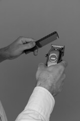 Barber holds in his hands a clipper and a comb