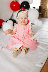 beautiful little one-year-old girl in a pink dress eats a lollipop. the child smeared himself with candy. kids love sweets