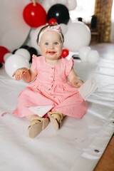 Fototapeta premium beautiful little one-year-old girl in a pink dress eats a lollipop. the child smeared himself with candy. kids love sweets