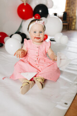 beautiful little one-year-old girl in a pink dress eats a lollipop. the child smeared himself with candy. kids love sweets