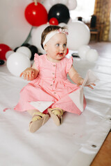 beautiful little one-year-old girl in a pink dress eats a lollipop. the child smeared himself with candy. kids love sweets