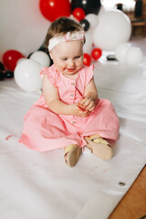 beautiful little one-year-old girl in a pink dress eats a lollipop. the child smeared himself with candy. kids love sweets