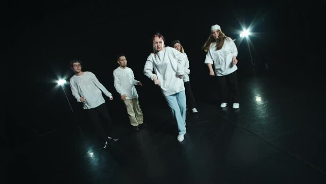A team of professional dancers perform on stage with hip hop. They are wearing similar clothes. Five people move their whole body to the beat of the music
