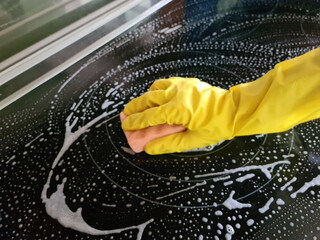 Cleaning induction hob. Woman in yellow rubber gloves cleans kitchen induction cooker with cleaning...