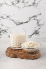 Glass cup of rice milk with a bowl of rice on a light background