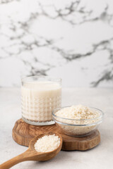 Glass cup of rice milk with a bowl of rice on a light background
