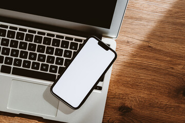 Mobile phone with blank white mockup touchscreen and laptop computer on office desk, top view