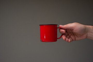 Red enameled tin camping cup or mug held in hand by a Caucasian male. Close up studio shot,...