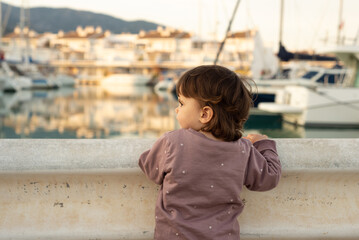 Female toddler looking at the boats on a mediterranean harbour at sunset.