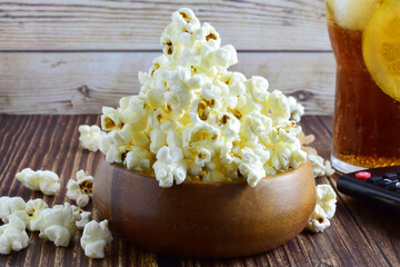 Wooden bowl with popcorn and soda next to it.
Rustic brown wooden table.